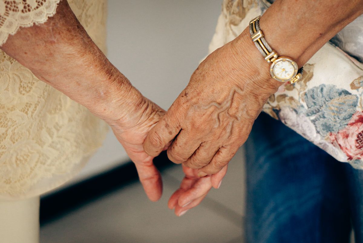Close view of two older hands resting together, a gold watch on one wrist.